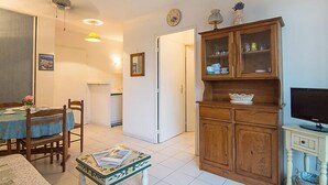 Un comedor con una mesa dispuesta para dos, un mueble de madera con puertas de cristal y un televisor sobre un soporte.