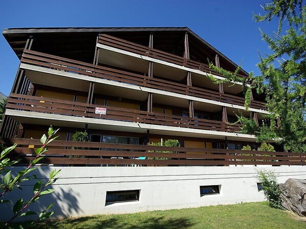 Un edificio de varios pisos con balcones, un letrero que indica una oferta y una pared blanca con dos ventanas pequeñas.