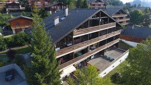A multi-story chalet with a sloped roof, wooden balconies, and a view of surrounding houses and mountains. - Zodiaque RS 4 by Interhome (Ovronnaz)
