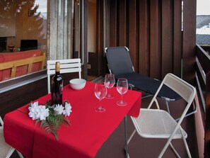 Een rode tafel met een fles en glazen, een witte stoel en een houten achtergrond.