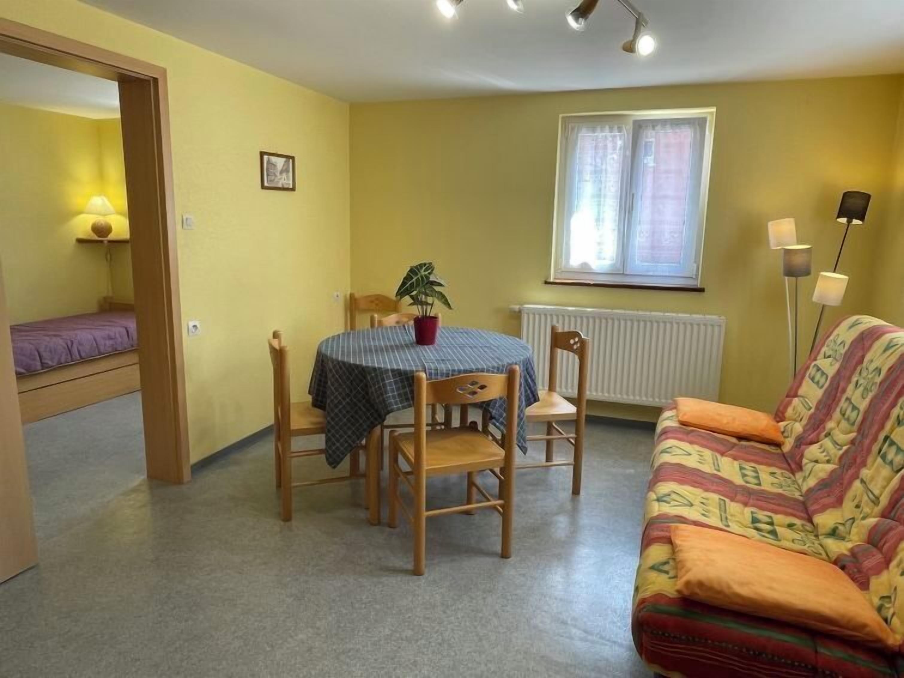 Un espace de vie compact comprenant une table à manger, des chaises, un canapé, une plante en pot et une fenêtre avec des rideaux.