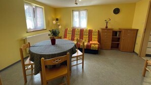 Een knus woongedeelte met een ronde eettafel, twee houten stoelen, een bank, een houten kast en een radiator.