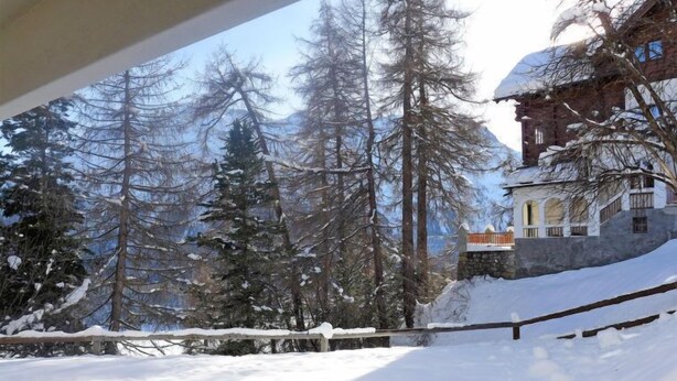 A snow-covered landscape with tall trees and a building with a stone wall and a balcony. - Chesa Cripels II by Interhome (St. Moritz)