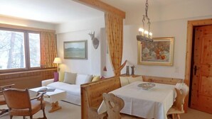 A cozy room with a wooden dining table, a sofa, and a chair. There is a painting on the wall and a window with curtains. - Chesa Cripels II by Interhome (St. Moritz)