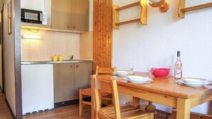 Kompakti keittiö, jossa on mikroaaltouuni, kaappeja ja ruokailutila, jossa on pöytä kahdelle.