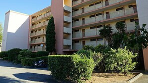 Un edificio a più piani con balconi, circondato da siepi curate e uno scooter parcheggiato.