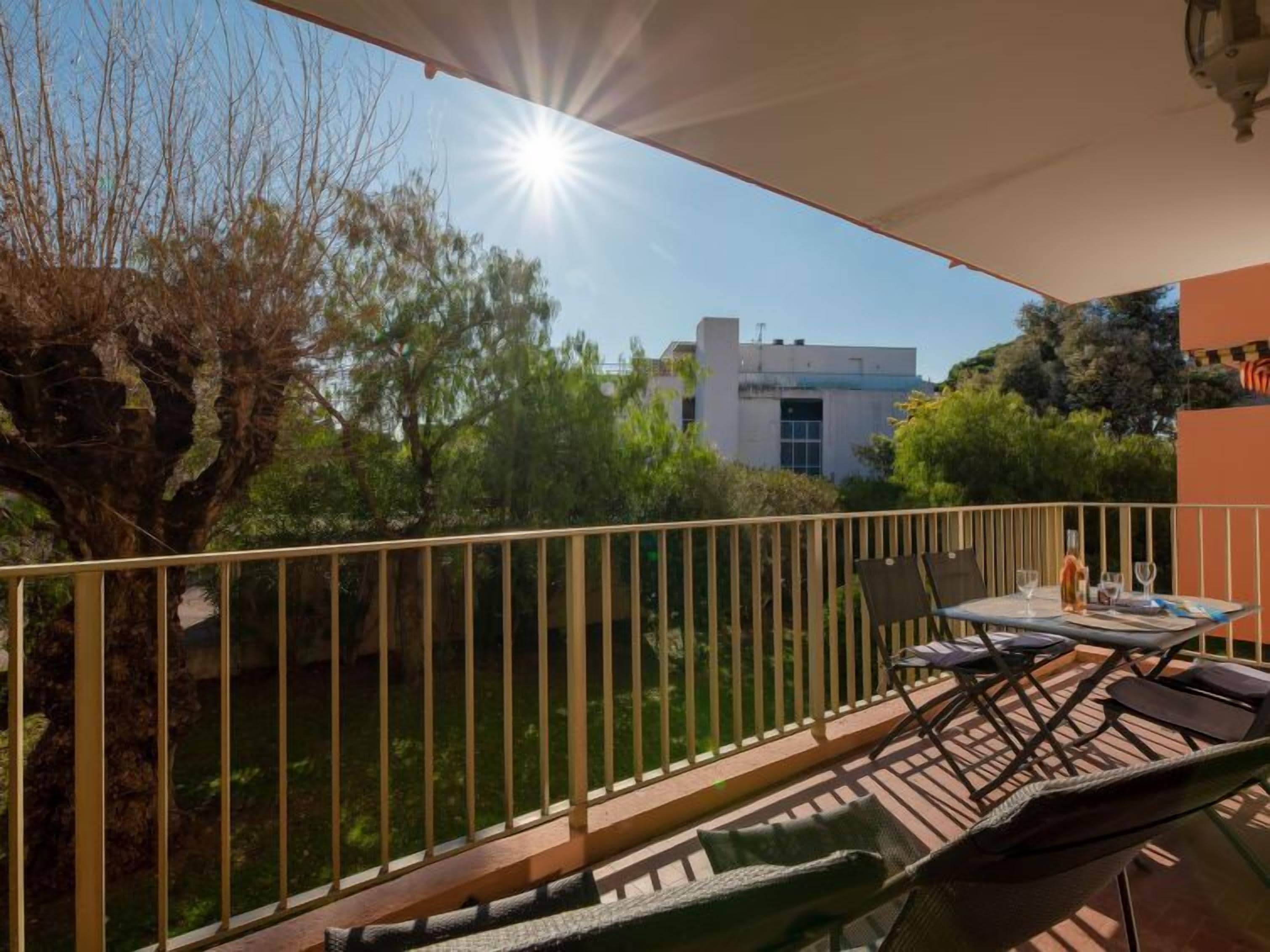 A balcony with a table and chairs, overlooking a garden and a building.