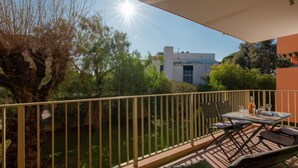 Un balcone con tavolo e sedie, affacciato su un giardino e un edificio.