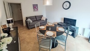 Un soggiorno moderno con un tavolo da pranzo per quattro persone, un divano, una televisione e una sveglia appesa al muro.