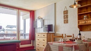 Una habitación acogedora con un aparador de madera, una mesa de comedor con copas de vino, un televisor en la pared y una ventana con cortina roja.