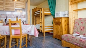 Cocina compacta con muebles de madera, una mesa de comedor con sillas, una cama litera y un sofá.
