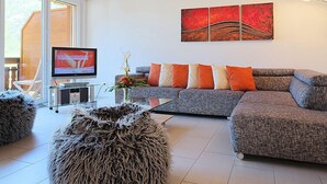 A modern living room with a grey sectional sofa, a flat-screen TV, and a glass coffee table. - Edelweiss A by Interhome (Leukerbad)