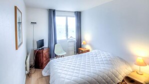 A hotel room with a bed, a desk, a chair, a TV, and a window with curtains.