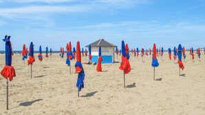 A beach with rows of red and blue umbrellas, a lifeguard hut, and a sandy beach.