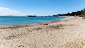 A beach with clear blue water, sandy shore, and distant hills.