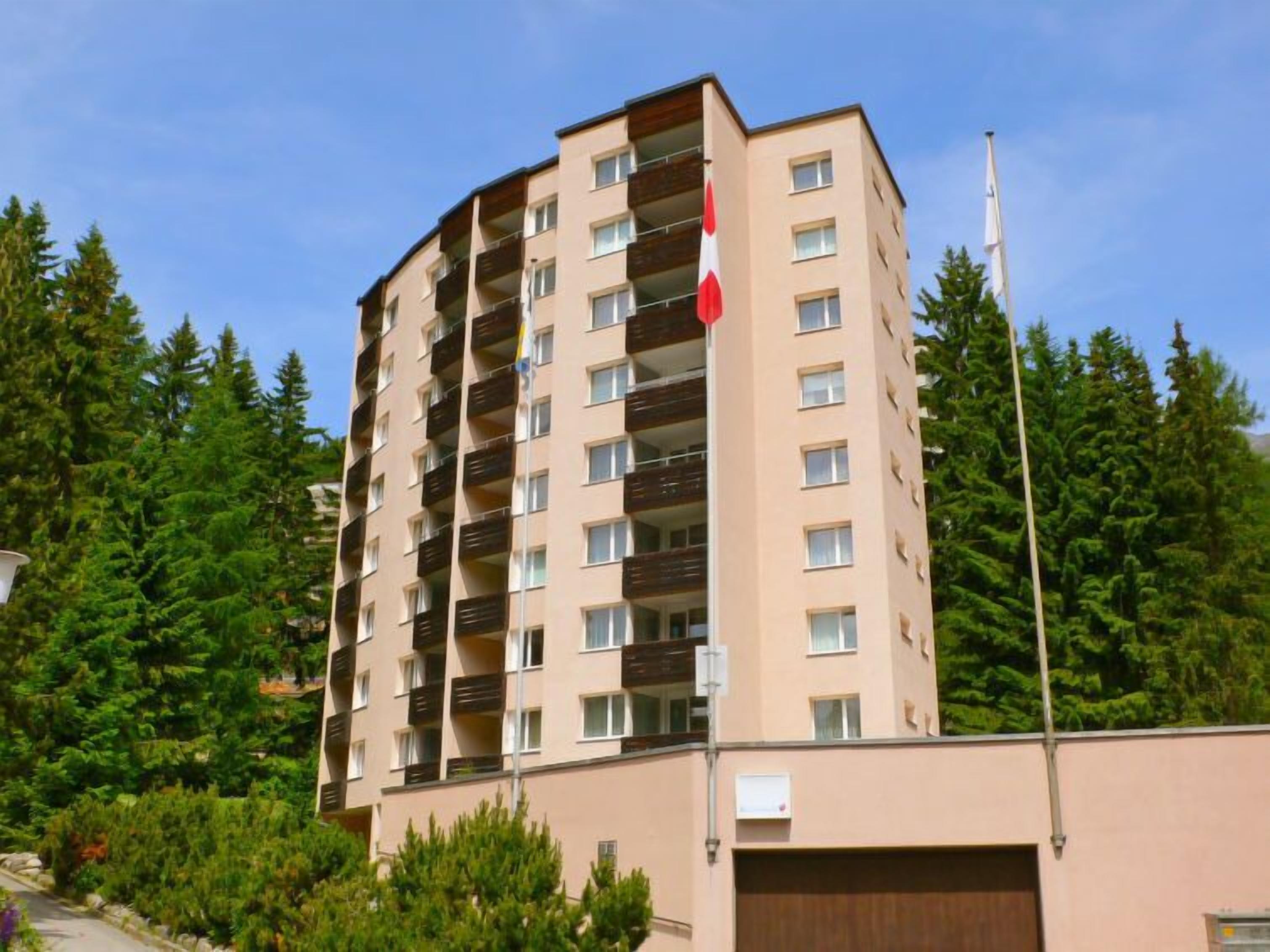 A multi-story residential building with balconies, surrounded by dense greenery.