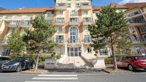 A multi-story hotel with a central entrance, balconies on each floor, and a parking area with cars. - Port Guillaume by Interhome (Cabourg)