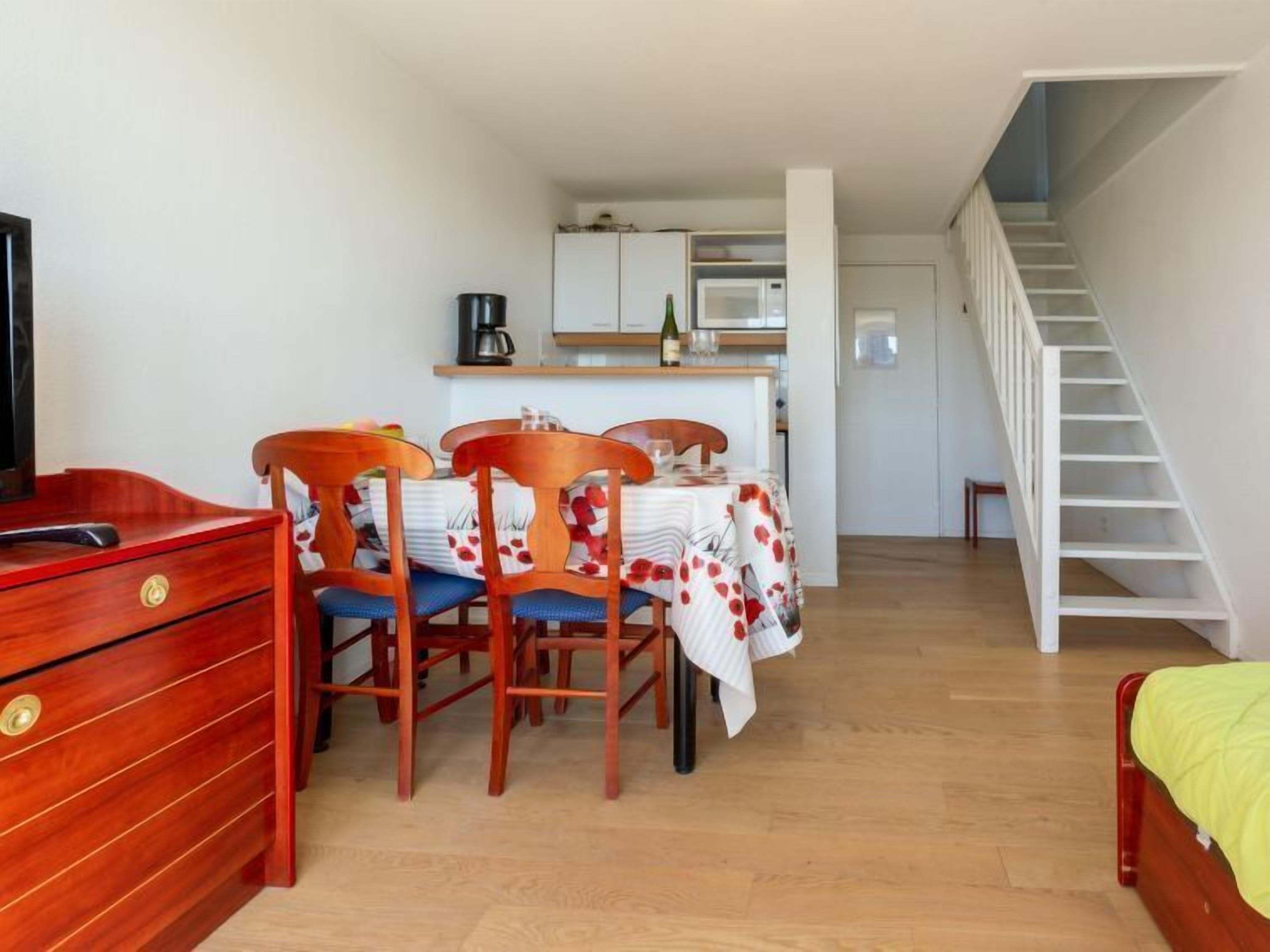 Een compacte kamer met een houten dressoir, een eettafel met stoelen, een bed, een keuken met kasten en een trap.