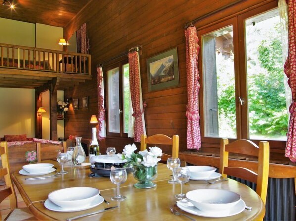 A wooden dining room with a table set for four, featuring white plates, glasses, and a vase with flowers.