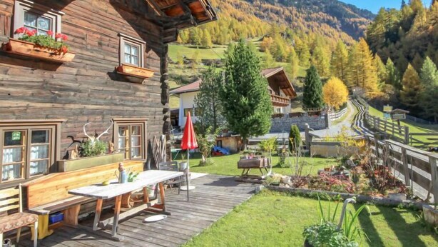 Eine Holzhütte mit Terrasse, Sitzgelegenheit im Freien und Blick auf eine gebirgige Landschaft.