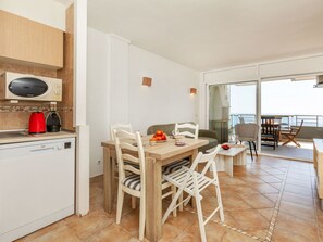 Une cuisine moderne équipée d’un four à micro-ondes, d’une machine à café et d’un lave-vaisselle. Un coin repas est aménagé avec une table, des chaises et offre une vue sur la mer grâce à de grandes fenêtres.