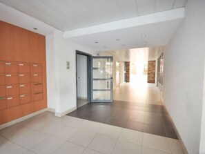 Un couloir avec des casiers sur le côté gauche, une porte en verre au centre et un mur de pierre sur le côté droit.