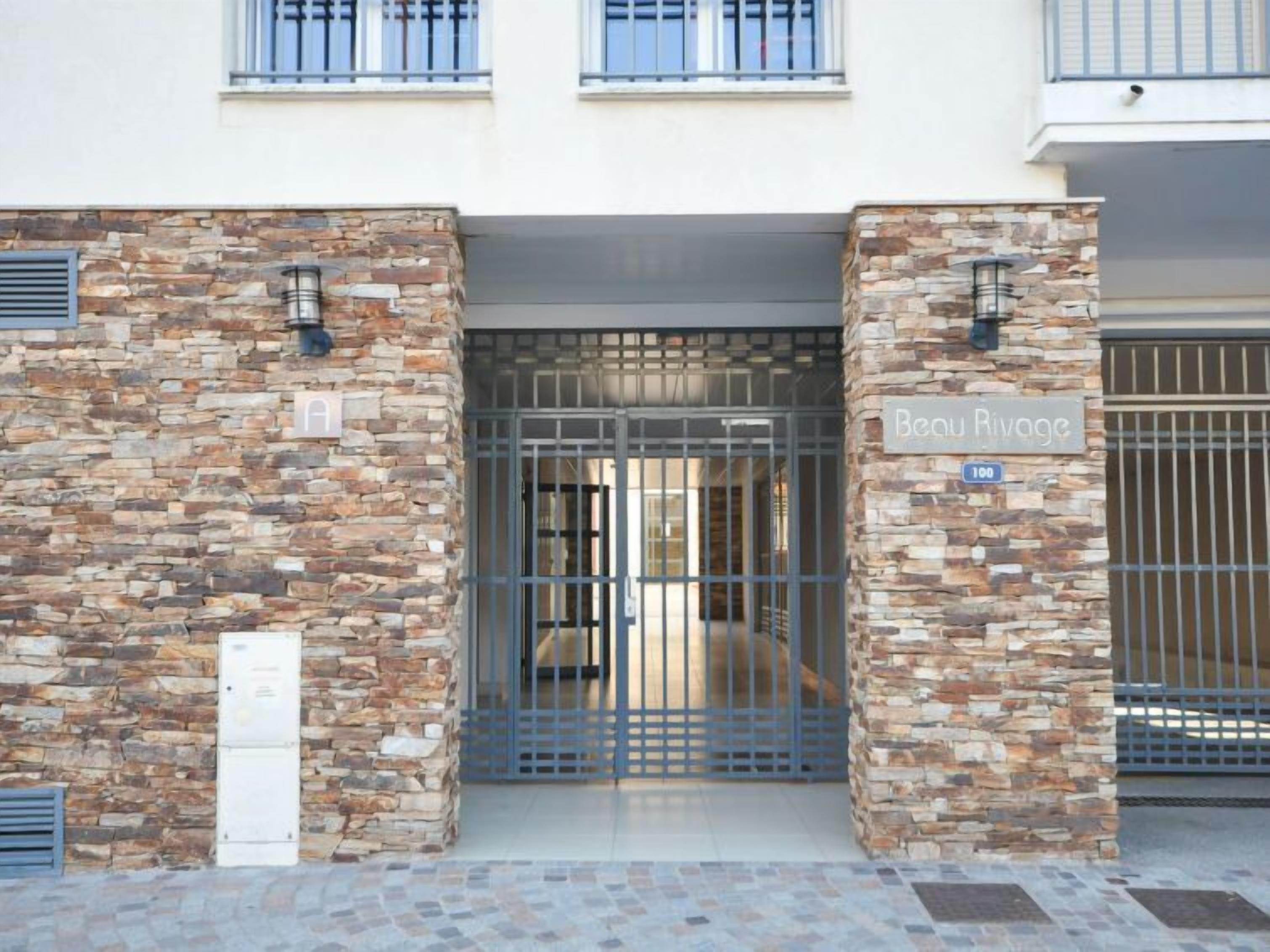 A building entrance with a stone facade, a metal gate, and a sign reading "Beau Rivage."
