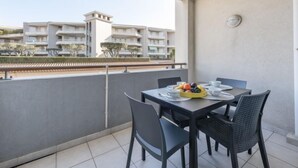Un balcon avec une table dressée pour deux personnes, agrémentée d’un panier de fruits et d’assiettes.