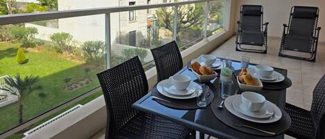 Un balcón con una mesa dispuesta para dos, sillas y vistas a un edificio y follaje.