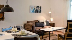 A cozy living room with a brown leather sofa, a dining table set with a white tablecloth, and a painting on the wall. - Chesa Ova Cotschna 205 by Interhome (St. Moritz)
