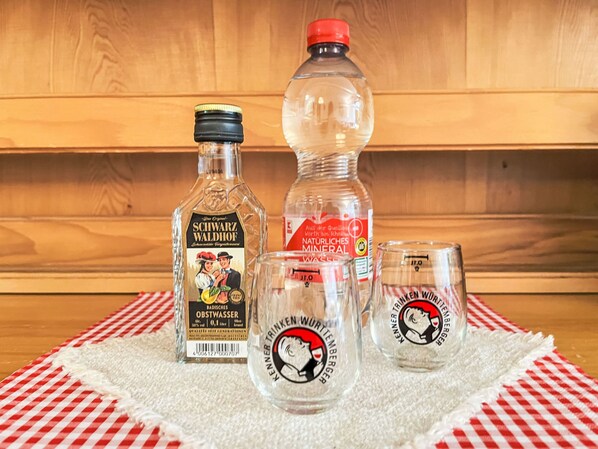 Une bouteille de Badisches Obstwasser, une bouteille d’eau minérale et deux verres ornés d’un logo, le tout posé sur une nappe à carreaux.