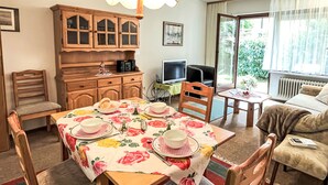 A cozy dining area with a table set for four, a wooden cabinet, a television, and a sofa by a window. - Sonnenmatt App. 12 by Interhome (Höchenschwand)