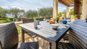 An outdoor patio with a table set for dining, surrounded by wicker chairs, and overlooking a garden with trees and a clear sky. - La Mesnière by Interhome (Vence)