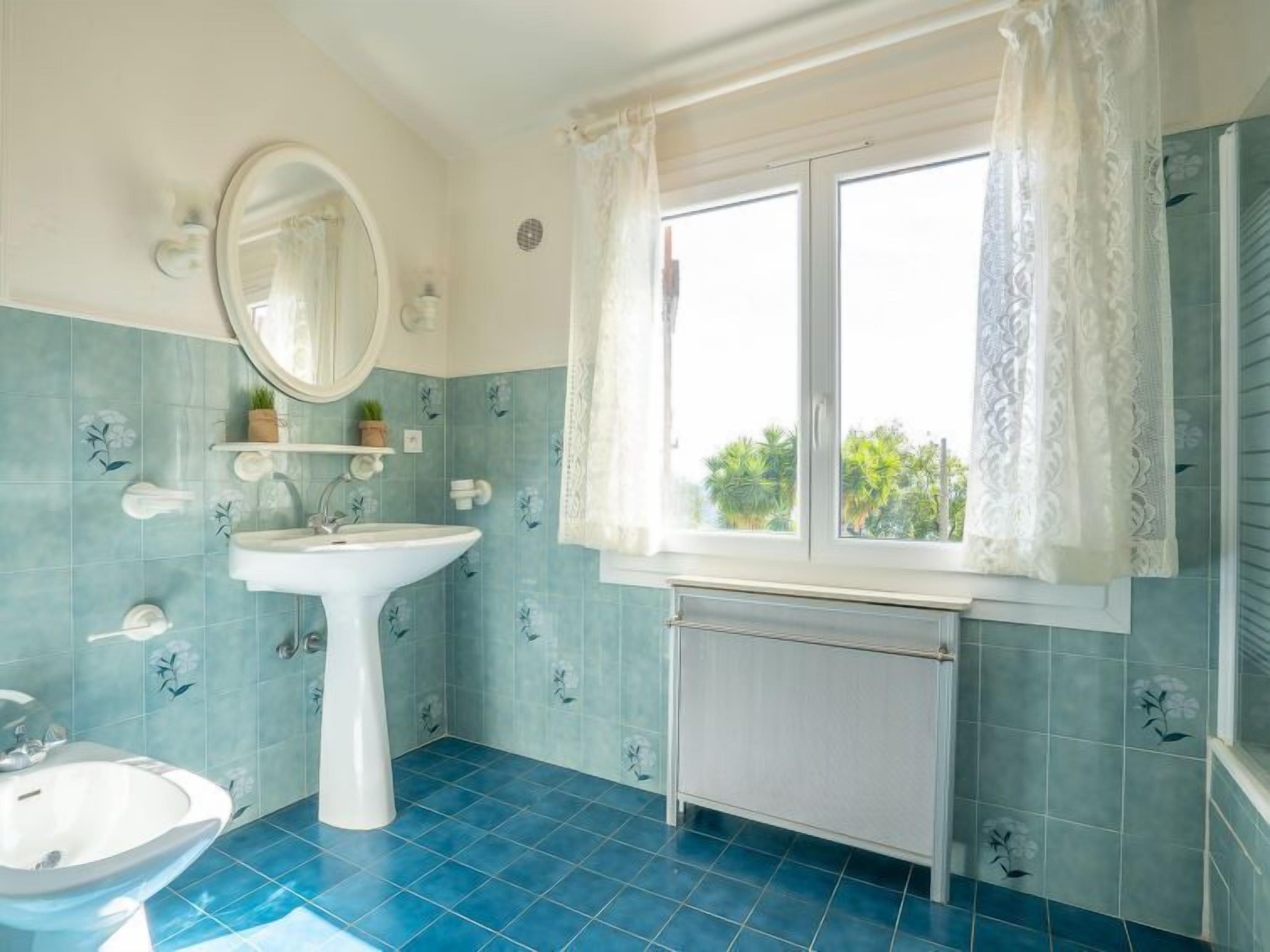 A bathroom with a white sink, a mirror, and a window with lace curtains.