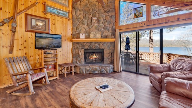 Ein gemütliches Blockhaus-Interieur mit Kamin aus Stein, Holzmöbeln, einem Fernseher und Seeblick.