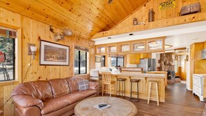 Ein Cabin-Innenraum mit Holzbalkendecke, einem Ledersofa, einem runden Holztisch, einer Küchenzeile mit Kamin aus Stein und einem Warnschild wegen Bären.
