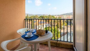 A balcony with a table set for two, a wicker basket, and a potted plant. - La Palmeraie II by Interhome (Sainte Maxime)