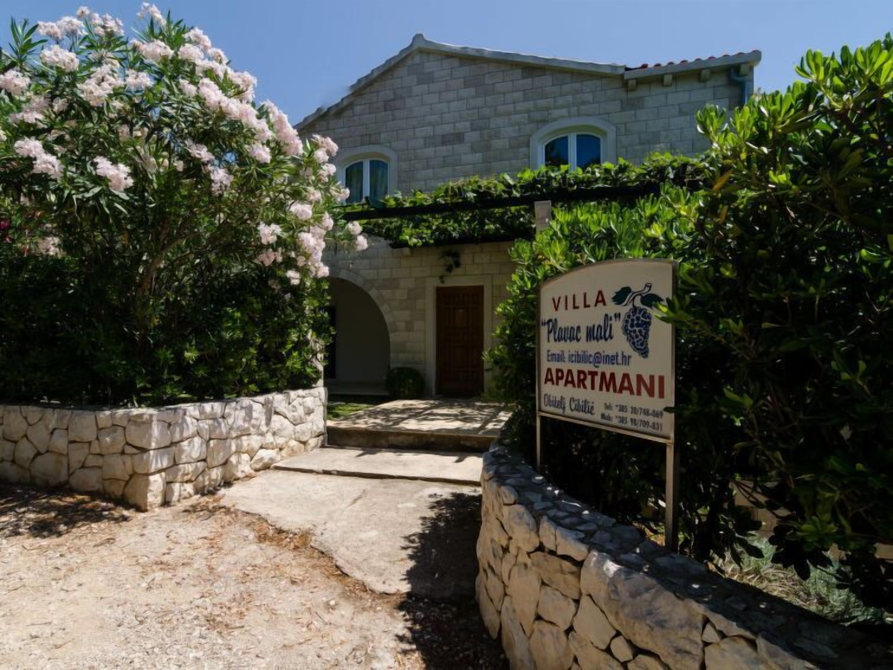 Una vila amb façana i mur de pedra, i un cartell publicitari d'apartaments.