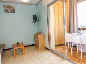 A room with a wooden table, a small cabinet, a TV mounted on the wall, and a dining area with a table and chairs.