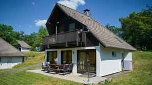 Una casa de dos pisos con un balcón, un patio con muebles de exterior y un jardín cubierto de césped.
