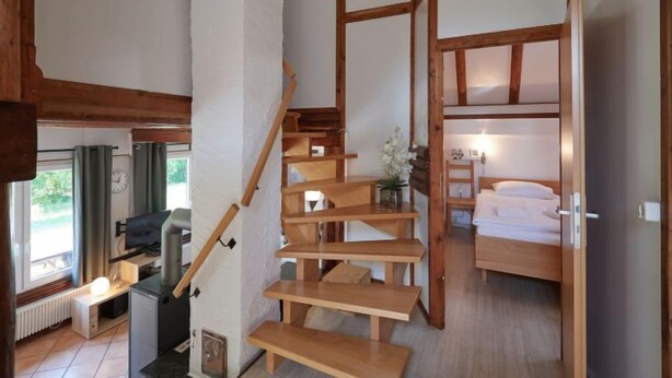 Habitación compacta con escalera de madera, literas, escritorio con silla y radiador.