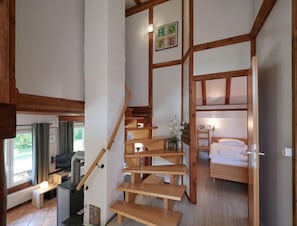 Une petite pièce avec un escalier en bois, un lit superposé, un bureau avec une chaise et un radiateur.