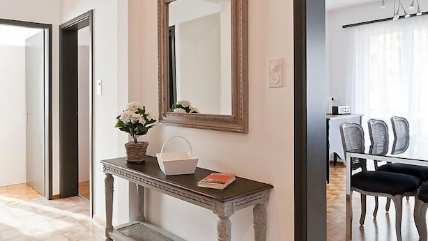 Un couloir agrémenté d’un miroir décoratif, une console sur laquelle sont posés un vase et un panier, et un coin repas avec des chaises et une table.