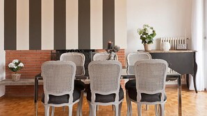 Un coin repas agrémenté d’une cheminée en briques, de chaises en osier blanches, d’une table noire et d’un luminaire suspendu.