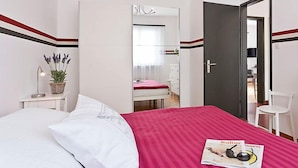Une chambre d’hôtel avec un lit, une table de chevet avec une lampe et une plante, un miroir, une porte et une chaise.