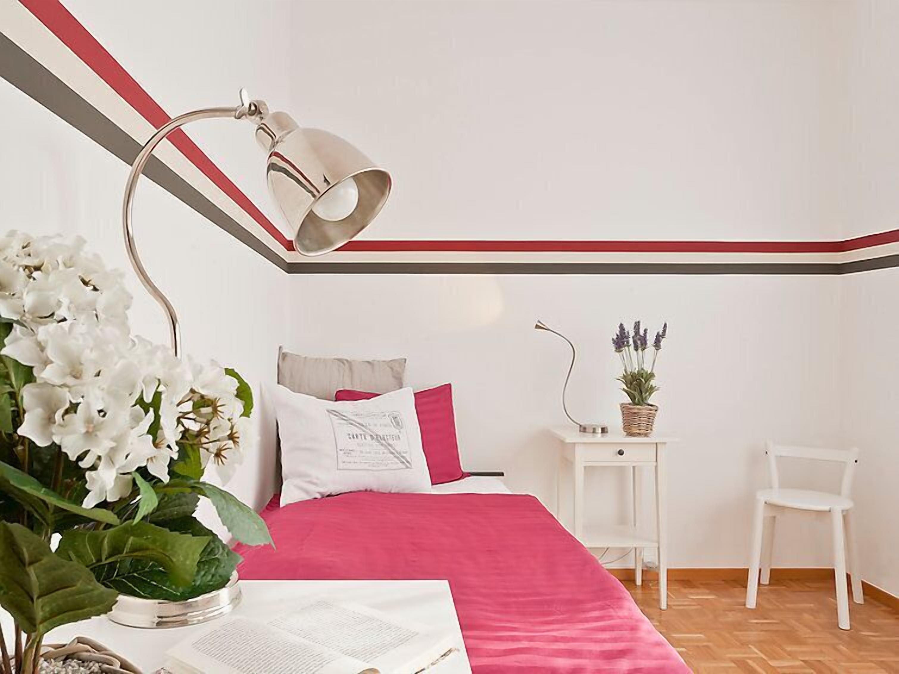 A bedroom with a bed, a bedside table with a lamp, a chair, and a small potted plant.