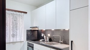 Una cocina compacta con armarios blancos, encimera negra, horno empotrado y pileta.