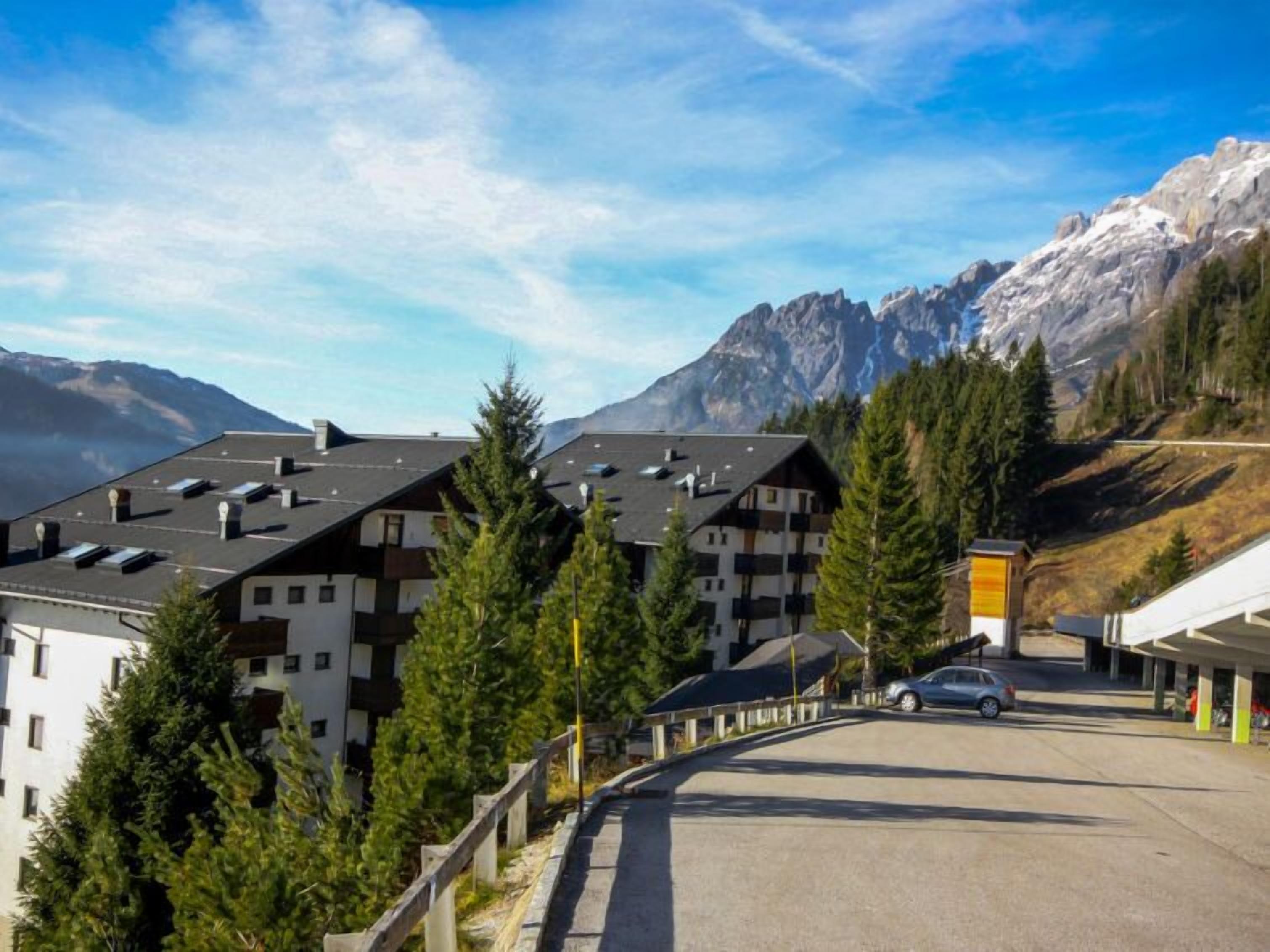 A mountain resort with chalet-style buildings, a parking area, and a view of snow-capped peaks.