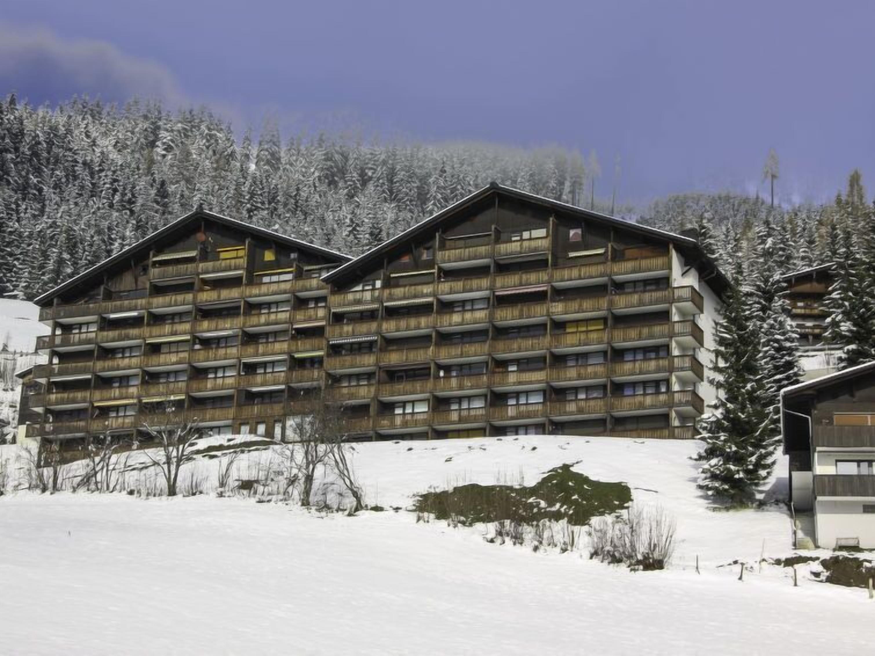 Um hotel com vários andares e varandas, situado em uma paisagem nevada com árvores.