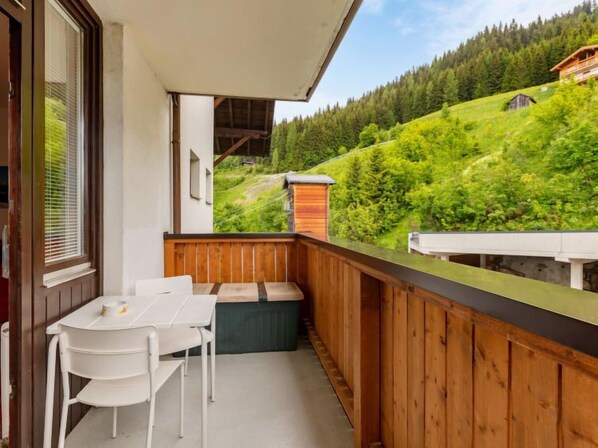 A balcony with a wooden railing, a white table, and two white chairs.